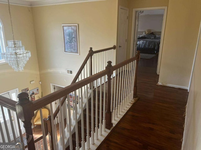hall with an upstairs landing, visible vents, baseboards, wood finished floors, and an inviting chandelier