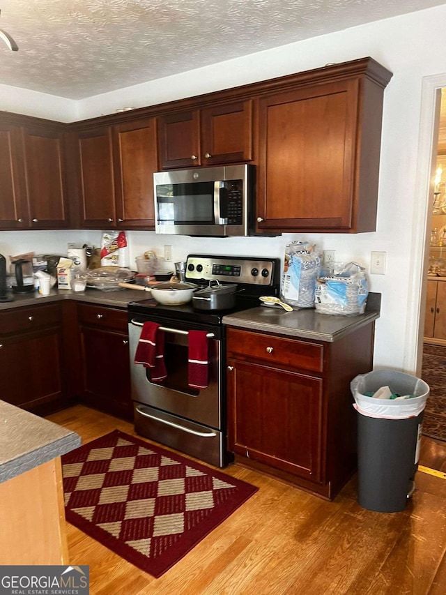 kitchen featuring a textured ceiling, dark countertops, light wood-style flooring, and stainless steel appliances