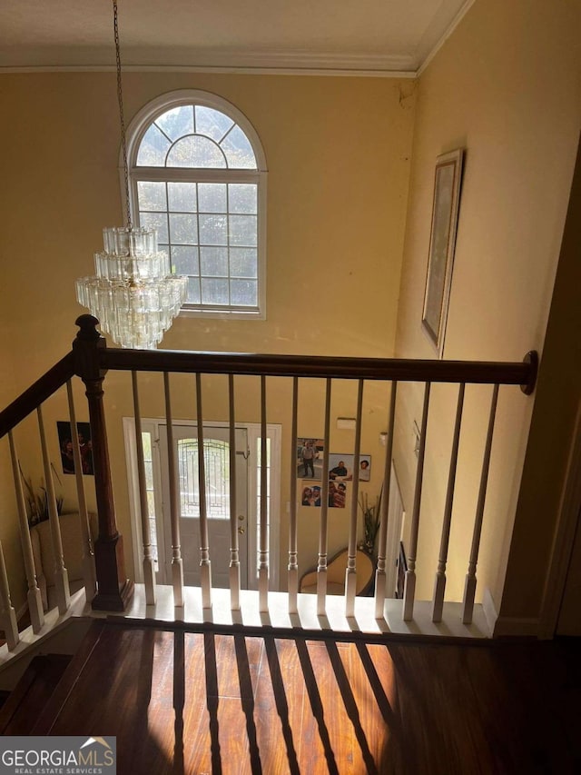 stairs with a notable chandelier, wood finished floors, crown molding, and a towering ceiling