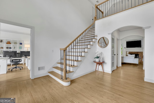 stairway with baseboards, arched walkways, visible vents, a fireplace, and wood finished floors