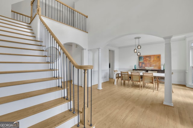 stairway with decorative columns, arched walkways, a high ceiling, and wood finished floors