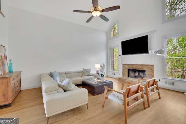 living area with high vaulted ceiling, light wood finished floors, visible vents, a ceiling fan, and a stone fireplace
