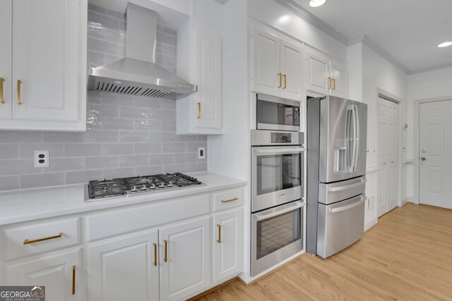 kitchen with wall chimney exhaust hood, stainless steel appliances, white cabinets, light wood-style floors, and decorative backsplash