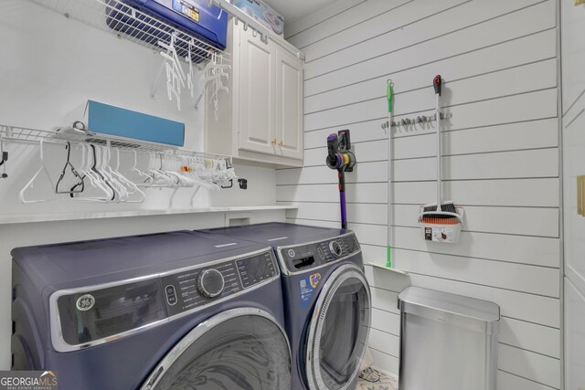 washroom featuring washing machine and dryer, wood walls, and cabinet space