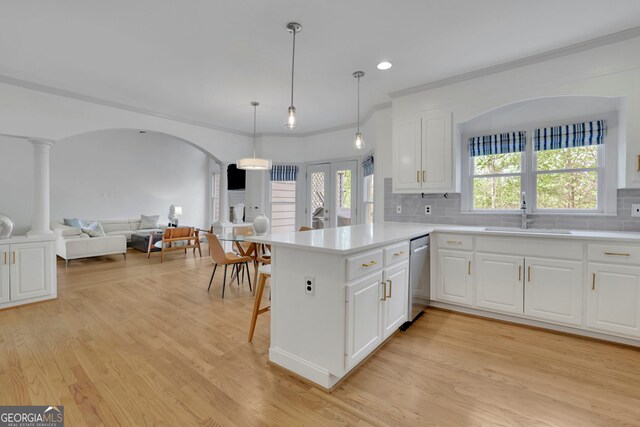kitchen featuring light wood-style flooring, a peninsula, dishwasher, a sink, and backsplash