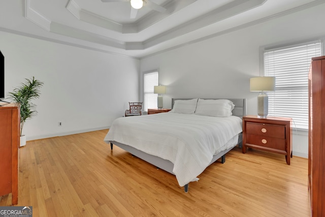 bedroom with a tray ceiling, a ceiling fan, light wood finished floors, baseboards, and ornamental molding