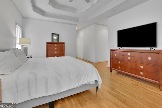 bedroom featuring a ceiling fan, a raised ceiling, ornamental molding, and wood finished floors