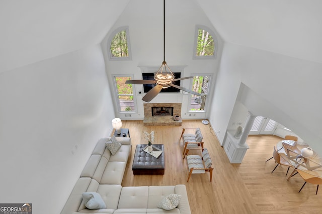 living room with a ceiling fan, a fireplace with raised hearth, high vaulted ceiling, and wood finished floors