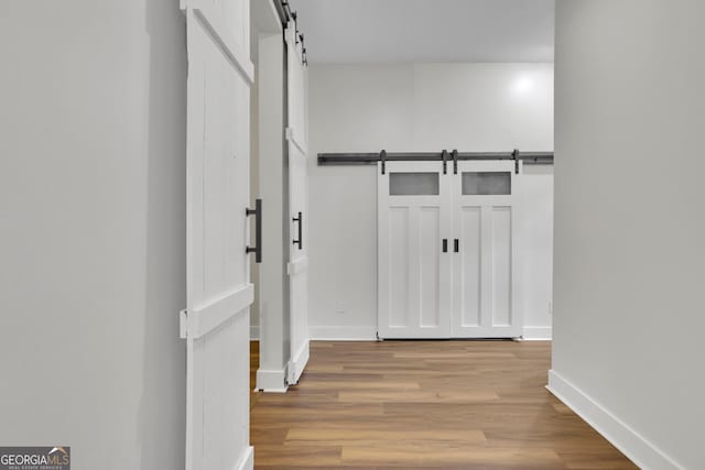 hall featuring baseboards, a barn door, and wood finished floors