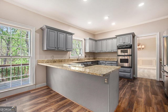 kitchen with dark wood finished floors, a peninsula, ornamental molding, stainless steel double oven, and gray cabinetry