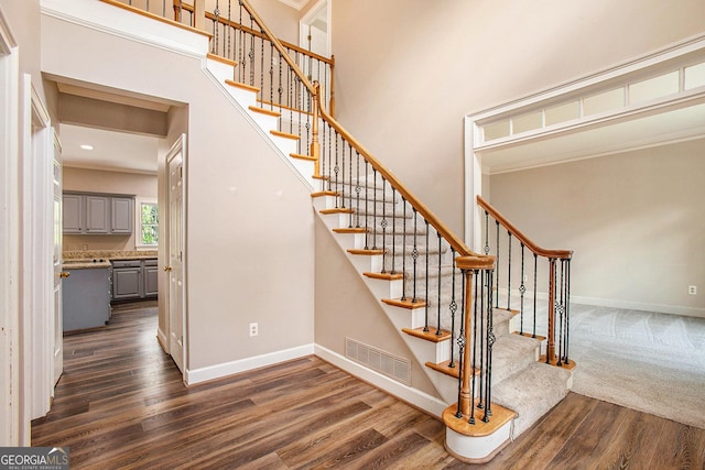 stairs featuring a towering ceiling, baseboards, crown molding, visible vents, and wood finished floors