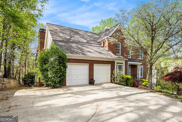 traditional-style house featuring roof with shingles, fence, brick siding, an attached garage, and concrete driveway