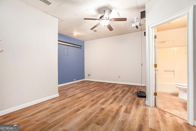 unfurnished bedroom featuring a paneled ceiling, a closet, baseboards, ensuite bathroom, and wood finished floors
