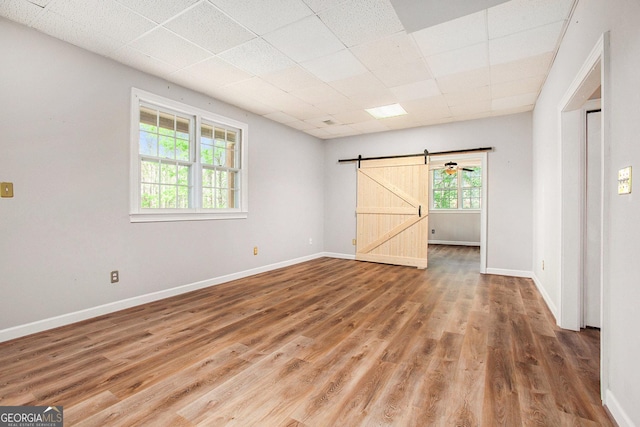 spare room featuring wood finished floors, baseboards, a drop ceiling, and a barn door