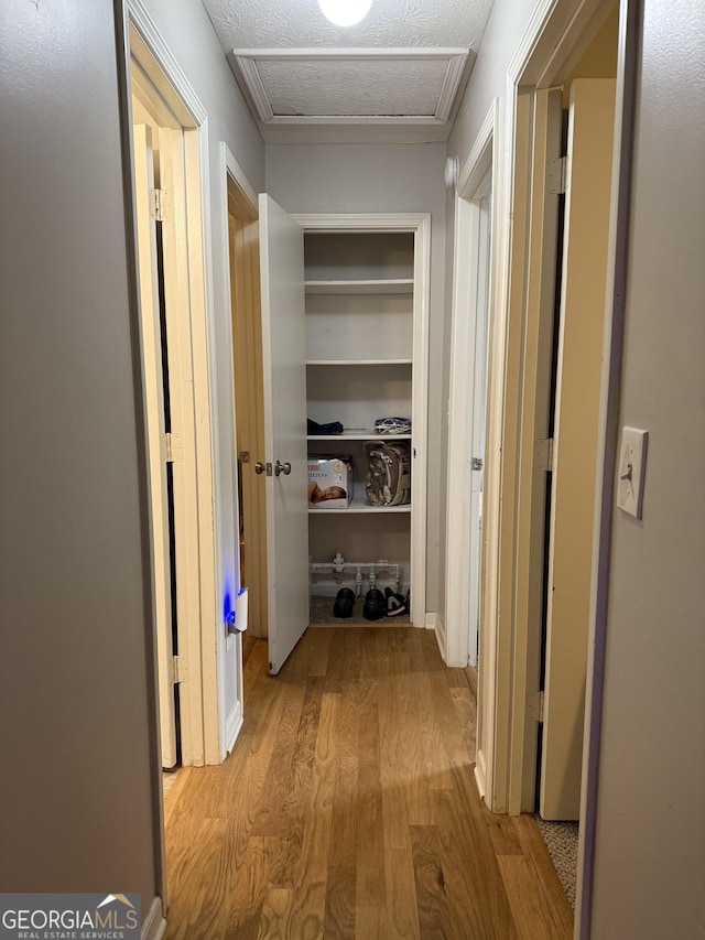 hall with a textured ceiling, attic access, and wood finished floors