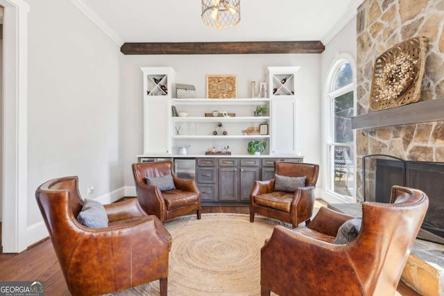 living area with an inviting chandelier, ornamental molding, baseboards, a stone fireplace, and wood finished floors