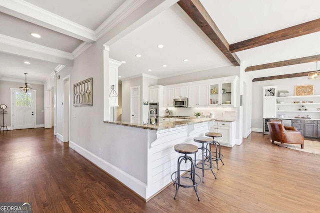 kitchen featuring white cabinetry, a kitchen bar, stainless steel microwave, beamed ceiling, and light stone countertops