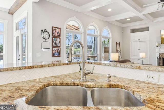 kitchen with coffered ceiling, beam ceiling, a sink, light stone countertops, and ornamental molding