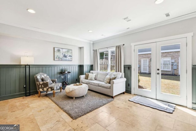 living room featuring a wainscoted wall, visible vents, ornamental molding, and french doors
