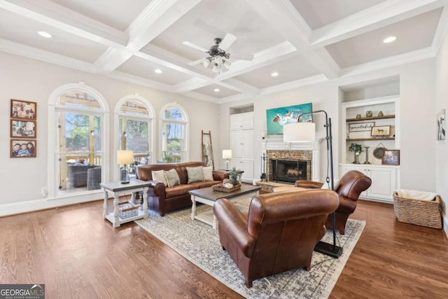 living room featuring coffered ceiling, built in shelves, wood finished floors, a stone fireplace, and beamed ceiling