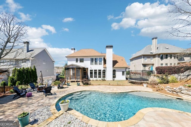view of pool featuring a patio area, a trampoline, an outdoor fire pit, fence, and a sunroom