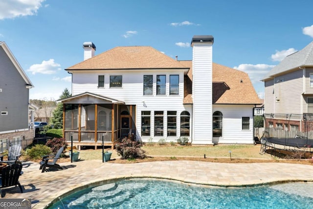 rear view of property with a patio, a chimney, a sunroom, and a trampoline
