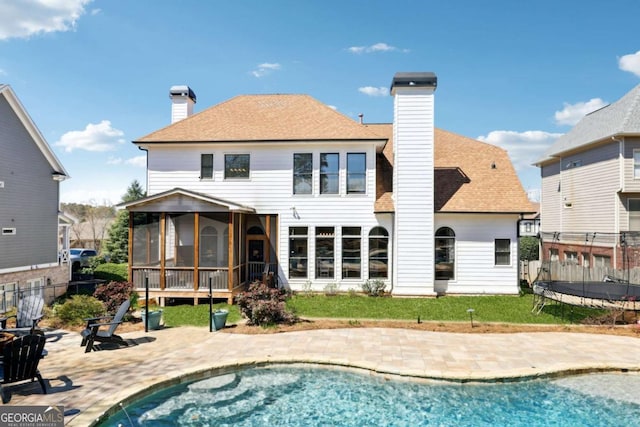 rear view of house with a trampoline, a sunroom, a patio area, and a chimney