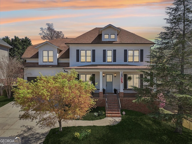 american foursquare style home with covered porch and a shingled roof