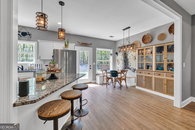 kitchen with freestanding refrigerator, light wood finished floors, a breakfast bar area, white cabinets, and dark stone counters