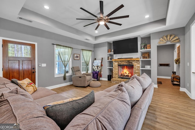 living room with light wood-type flooring, a raised ceiling, visible vents, and ceiling fan