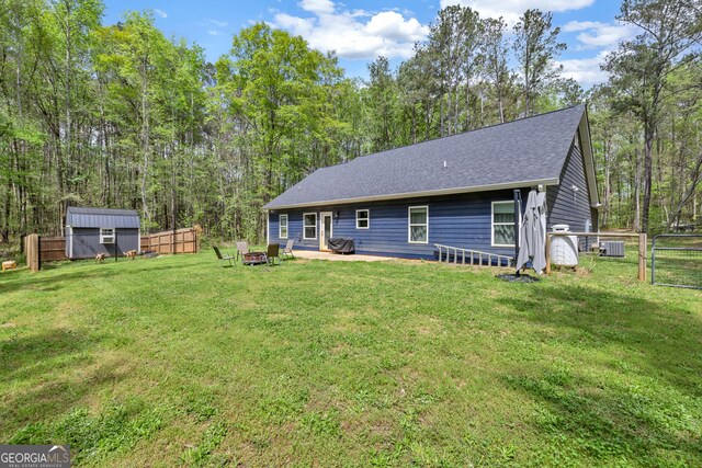 view of front of home featuring an outbuilding, roof with shingles, fence, a forest view, and a front yard