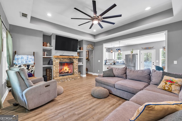 living room featuring a tray ceiling, light wood-style floors, and ceiling fan