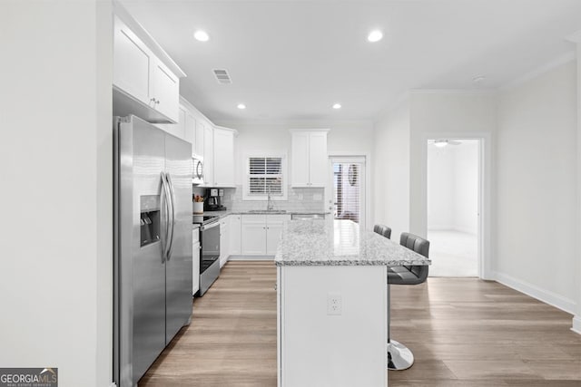 kitchen with visible vents, a kitchen bar, crown molding, a kitchen island, and appliances with stainless steel finishes