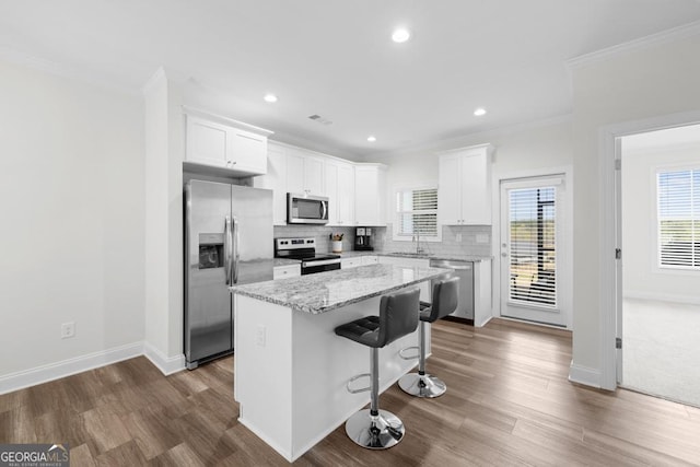 kitchen with a sink, stainless steel appliances, white cabinetry, ornamental molding, and a kitchen island
