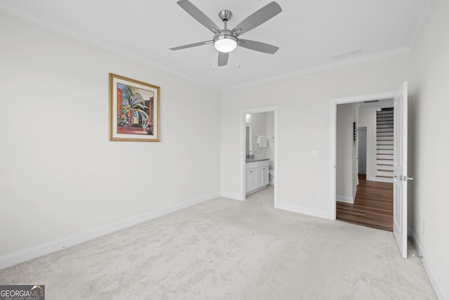 unfurnished bedroom featuring light carpet, ensuite bathroom, baseboards, ceiling fan, and crown molding