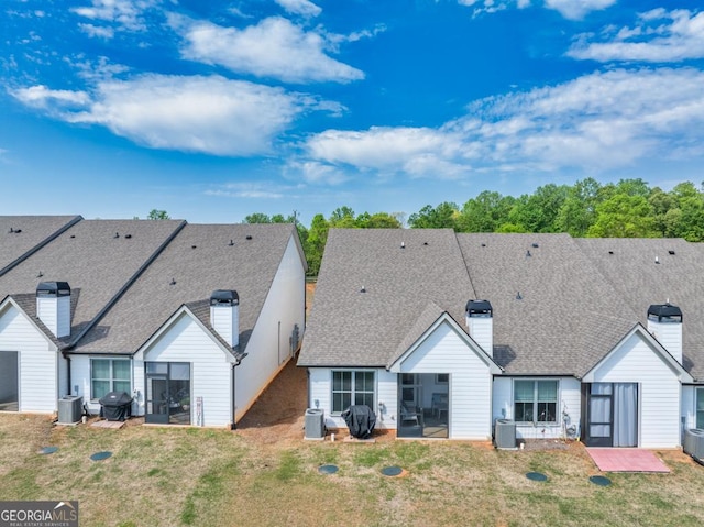 back of house with a sunroom, a chimney, central AC unit, and a lawn