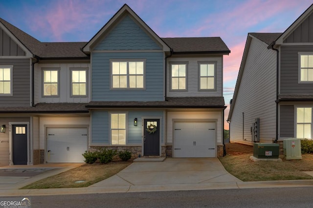 townhome / multi-family property featuring driveway, stone siding, board and batten siding, and a garage
