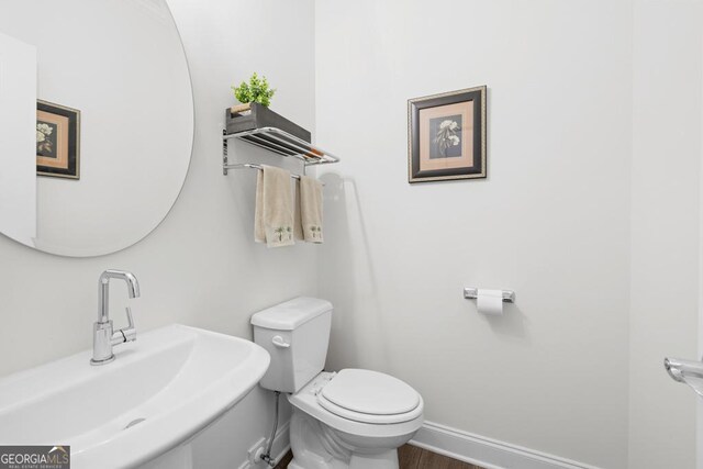 bathroom featuring wood finished floors, toilet, baseboards, and a sink