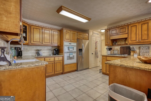 kitchen with a sink, stainless steel appliances, brown cabinetry, and tasteful backsplash