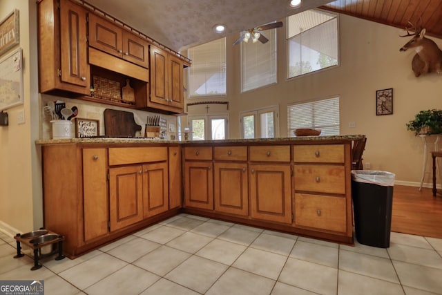 kitchen featuring a peninsula, light stone countertops, ceiling fan, brown cabinets, and vaulted ceiling