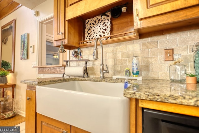 kitchen with baseboards, backsplash, a sink, light stone counters, and brown cabinets