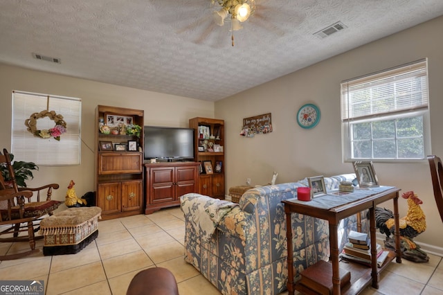 living area with a textured ceiling, visible vents, ceiling fan, and light tile patterned floors