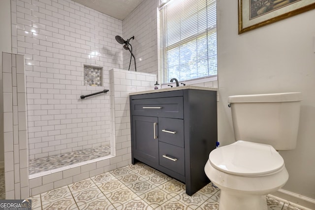 bathroom featuring toilet, tiled shower, tile patterned flooring, and vanity