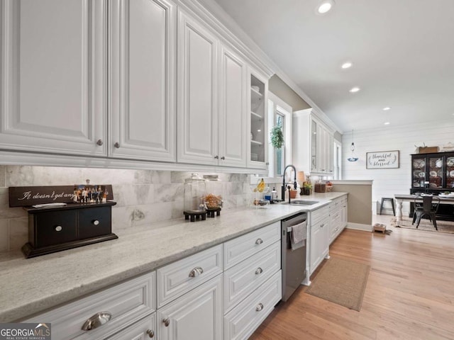 kitchen with white cabinetry, a sink, light wood finished floors, dishwasher, and glass insert cabinets