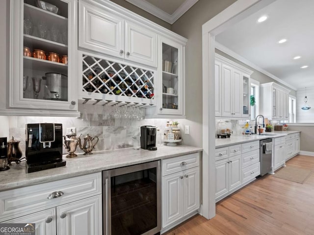 bar featuring crown molding, wine cooler, stainless steel dishwasher, a bar, and light wood-style flooring