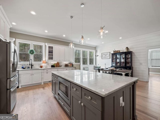 kitchen featuring light wood-type flooring, stainless steel appliances, a kitchen island, a sink, and white cabinets