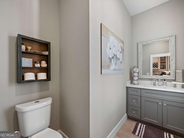 half bathroom with baseboards, wood finished floors, toilet, and vanity
