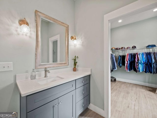 bathroom with vanity, wood finished floors, a walk in closet, baseboards, and recessed lighting