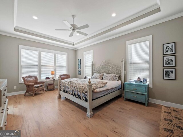 bedroom featuring baseboards, a tray ceiling, light wood-style flooring, and crown molding