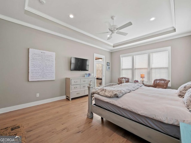 bedroom featuring a raised ceiling, ornamental molding, baseboards, and light wood-style floors